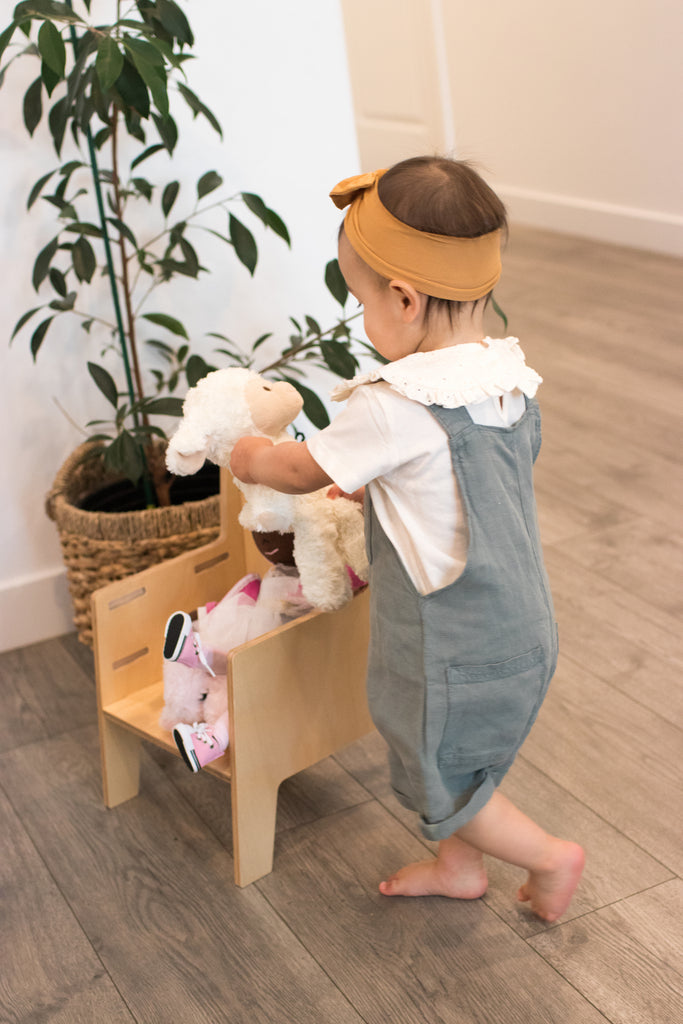 A little girl places several stuffed animals onto an adjustable Montessori chair for kids